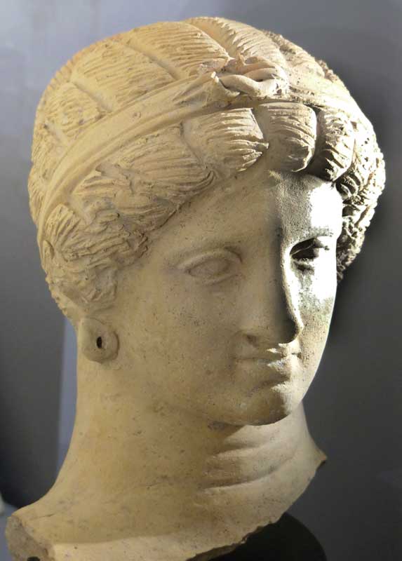 Tête de femme en terre cuite montrant un
                    diadème avec le noeud d'Héracles sur une coiffure
                    Melonfrisur courante dans le monde grec (fin du IVe.
                    av. J-C)