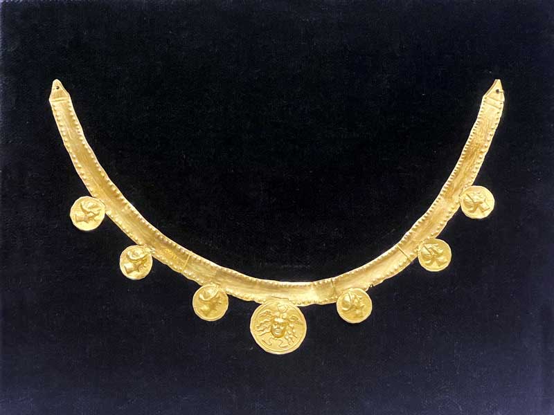 Collier en or consistant-en une plaque courbée en
                arc auquel sont attachés des disques décorés d'une tête
                de Méduse et de têtes de femmes (150-125 av. J.-C.)